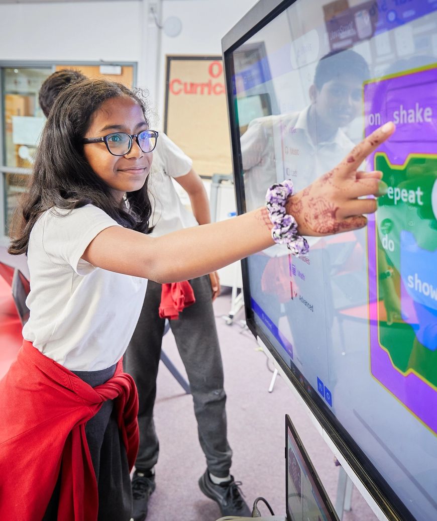 Female pupil in a primary school classroom pointing to block code on an interactive whiteboard